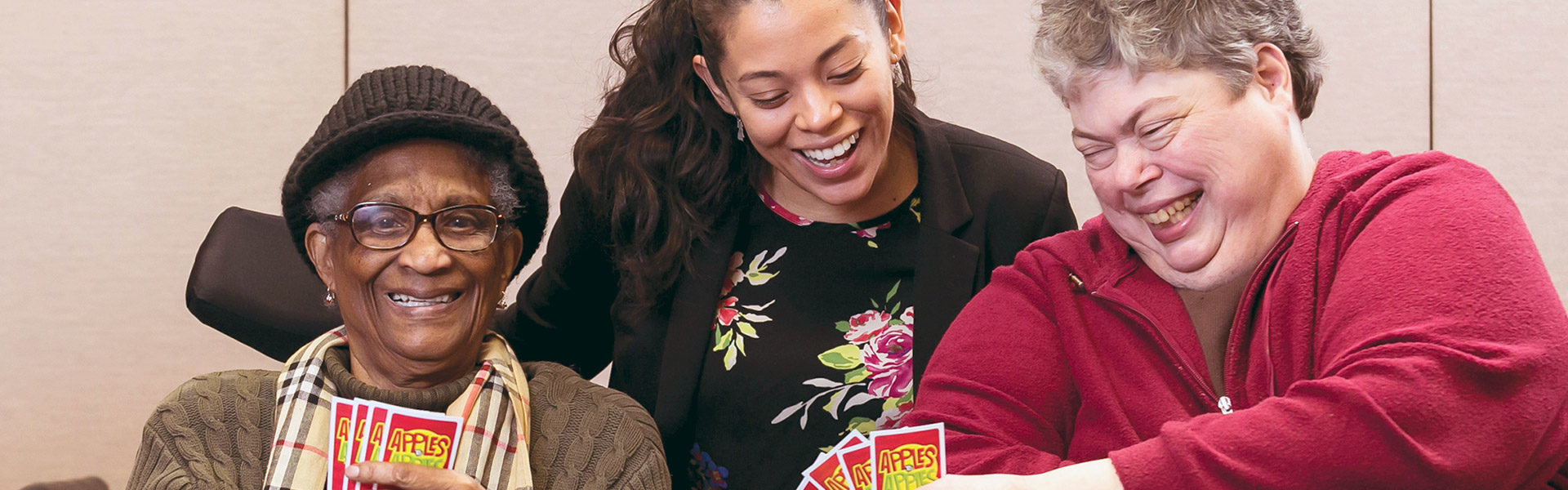 Young woman laughing playing a card game with two stroke survivors