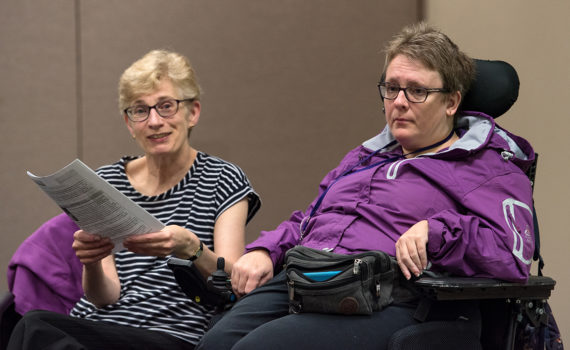 Woman holding list sitting beside woman in wheelchair